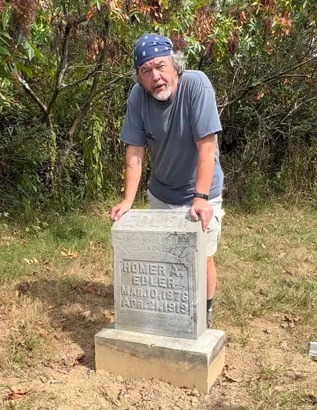 A man in a bandana standing by a gravestone